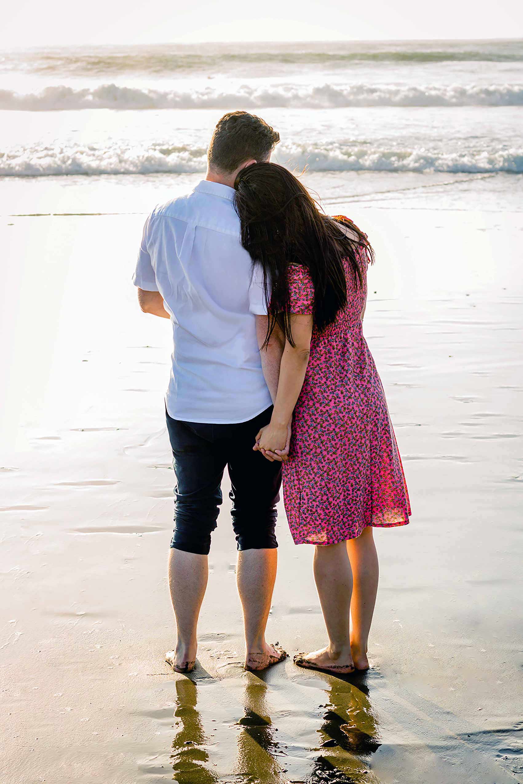 A couple walking hand in hand on a beach at sunset with a Bitcoin silhouette in the sea.