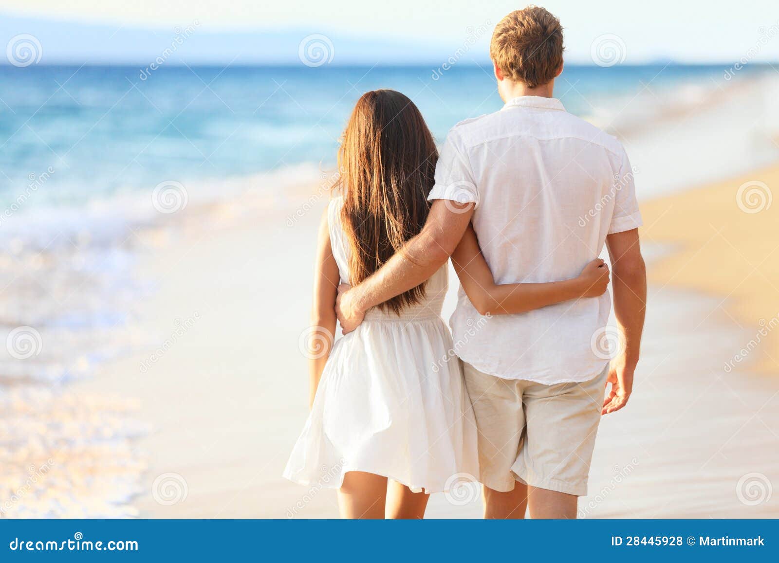 A couple walking hand in hand on a beach during sunset with vibrant sky colors.